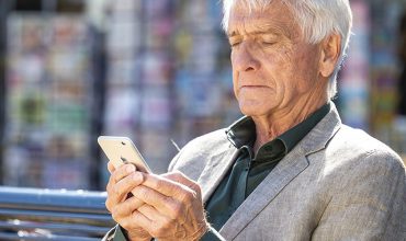 Oudere man op bankje kijkt vreemd naar mobiel